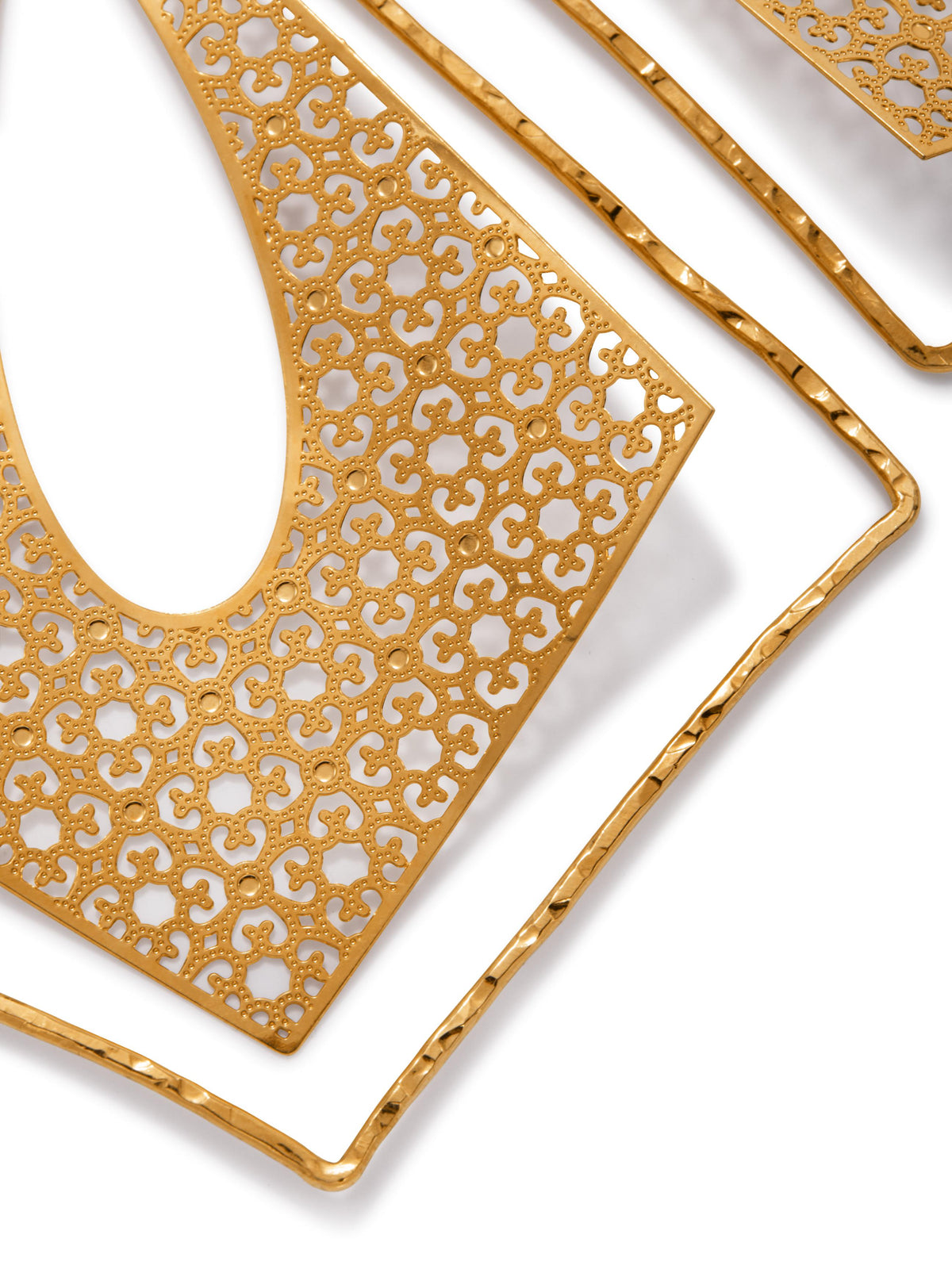 gros plan of the 18K plaqué or Tudor Temptations Leverback boucles d'oreilles, avec a teardrop cutout, symmetrical filigree pattern, et hammered square frame; these modern de luxe boucles d'oreilles cast élégant shadows sur un white surface.