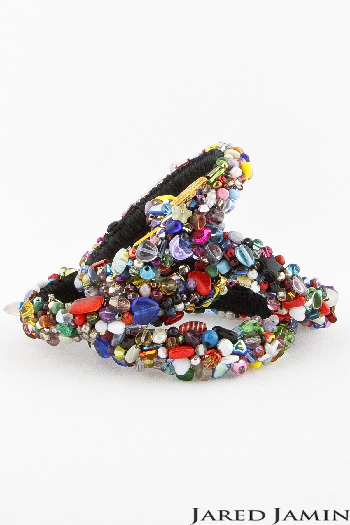 A pair of intricately beaded Candy Encrustation Bangles is shown against a plain white background. They are adorned with an array of colorful beads in various shapes and sizes, including red, blue, green, and white, creating a vibrant and ornate appearance. The brand name "JAREDJAMIN Jewelry Online" is displayed at the bottom. This exquisite piece exemplifies designer jewelry craftsmanship.