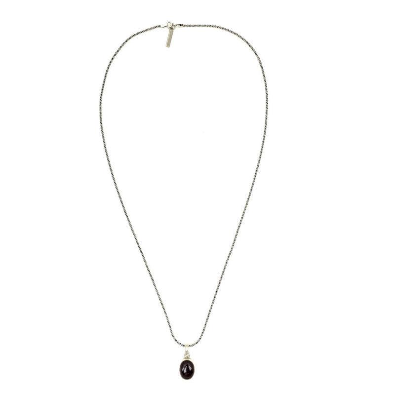 The Gage Garnet Necklace by JAREDJAMIN Jewelry Online features a delicate sterling silver chain with a small dark garnet pendant, elegantly displayed in an open loop with its secure hook clasp on a plain white background.